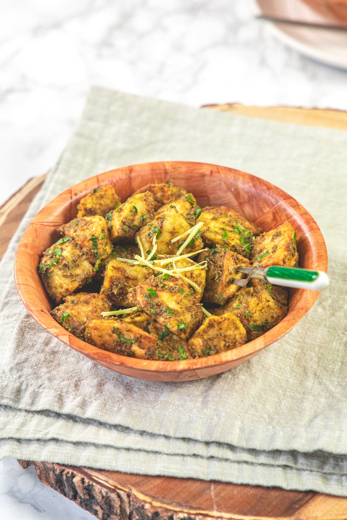 A bowl of aloo chaat garnished with julienned ginger and napkin under the bowl.