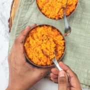 2 bowls of carrot halwa and taking spoonful of halwa from one bowl.