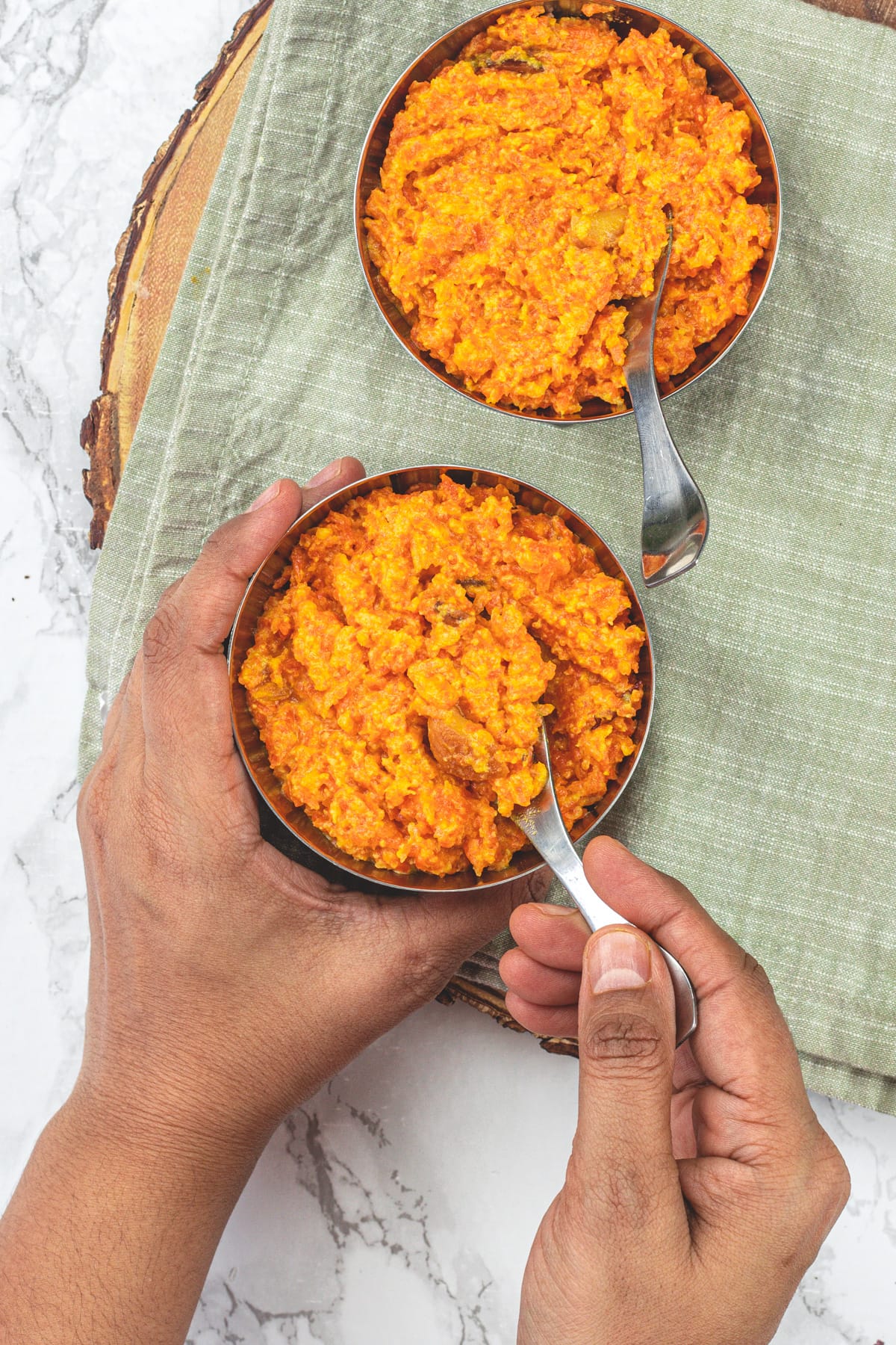 2 bowls of carrot halwa and taking spoonful of halwa from one bowl.