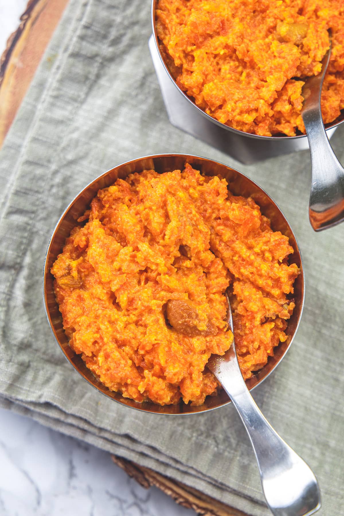 2 bowls of gajar halwa with spoons in the bowls and napkin under the bowls.