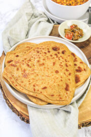 Tawa paratha on a plate with pickle in the back.