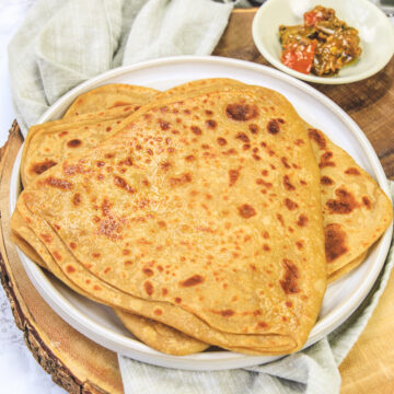 Tawa paratha on a plate with pickle in the back.
