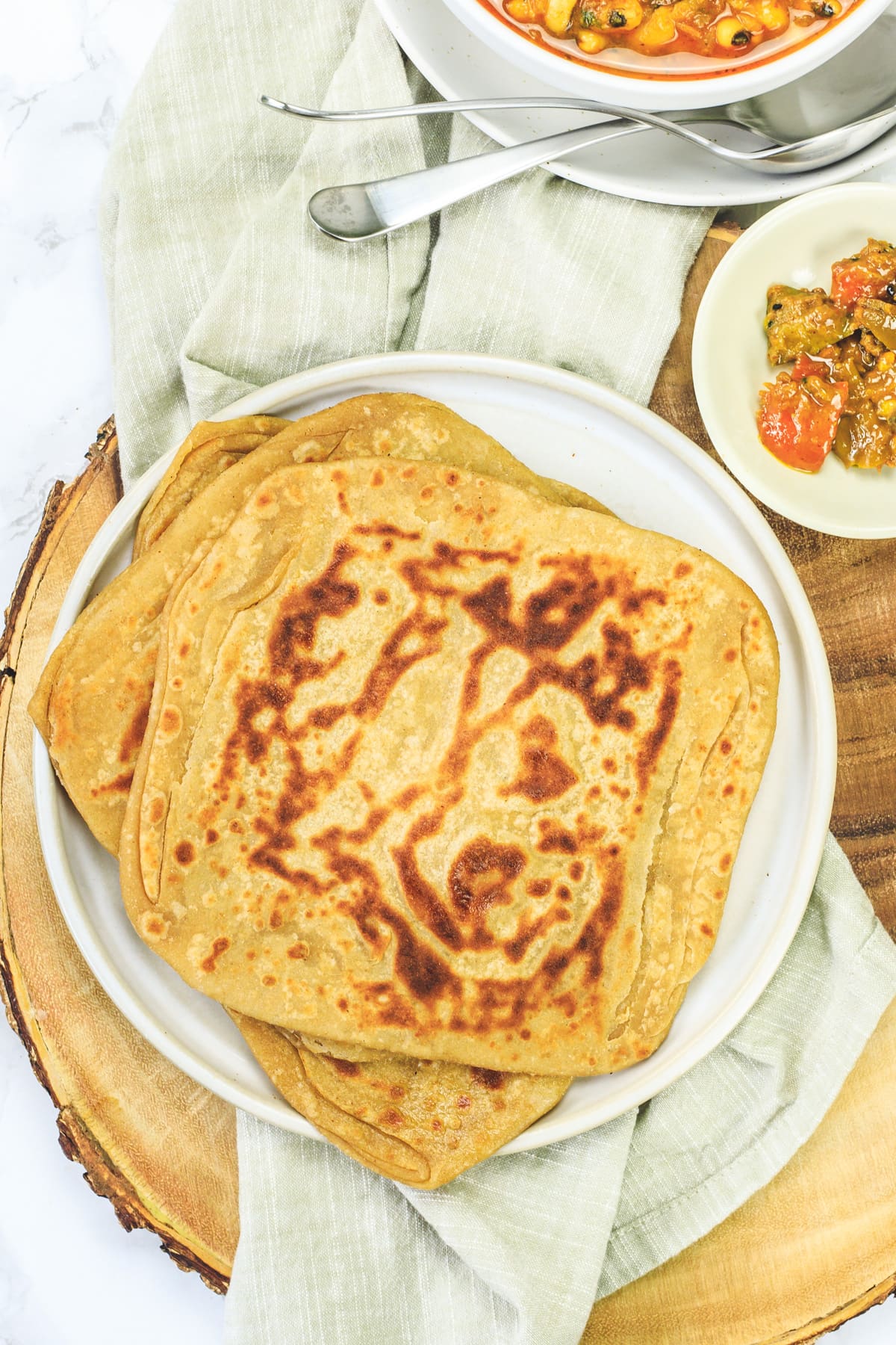 Plain paratha in a plate with napkin under the plate and pickle on the side.