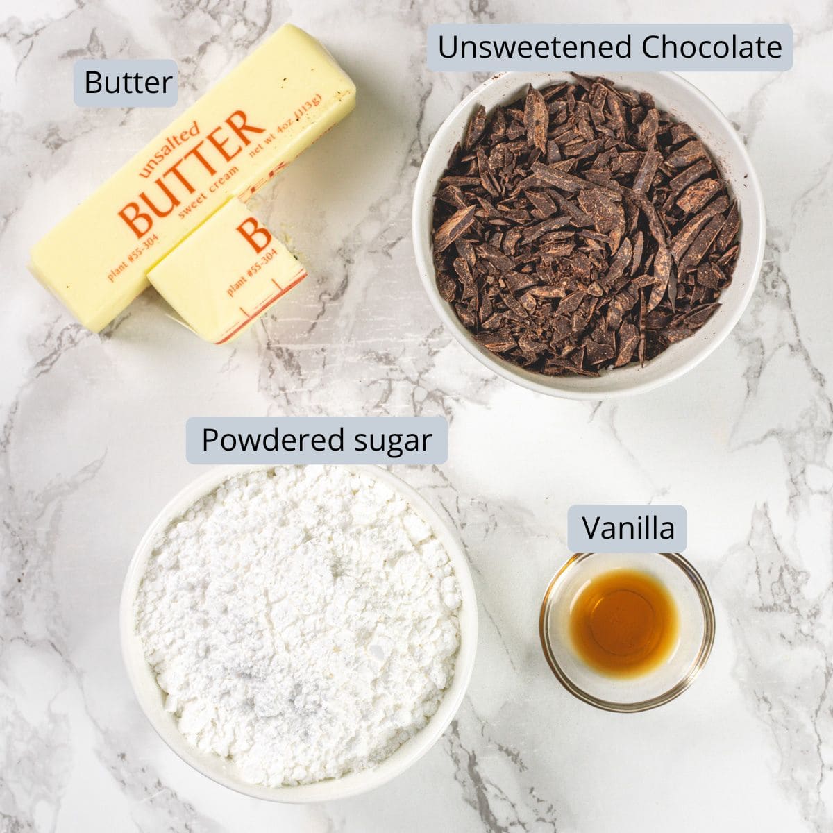 Chocolate buttercream frosting ingredients in bowls on a marble surface with labels.