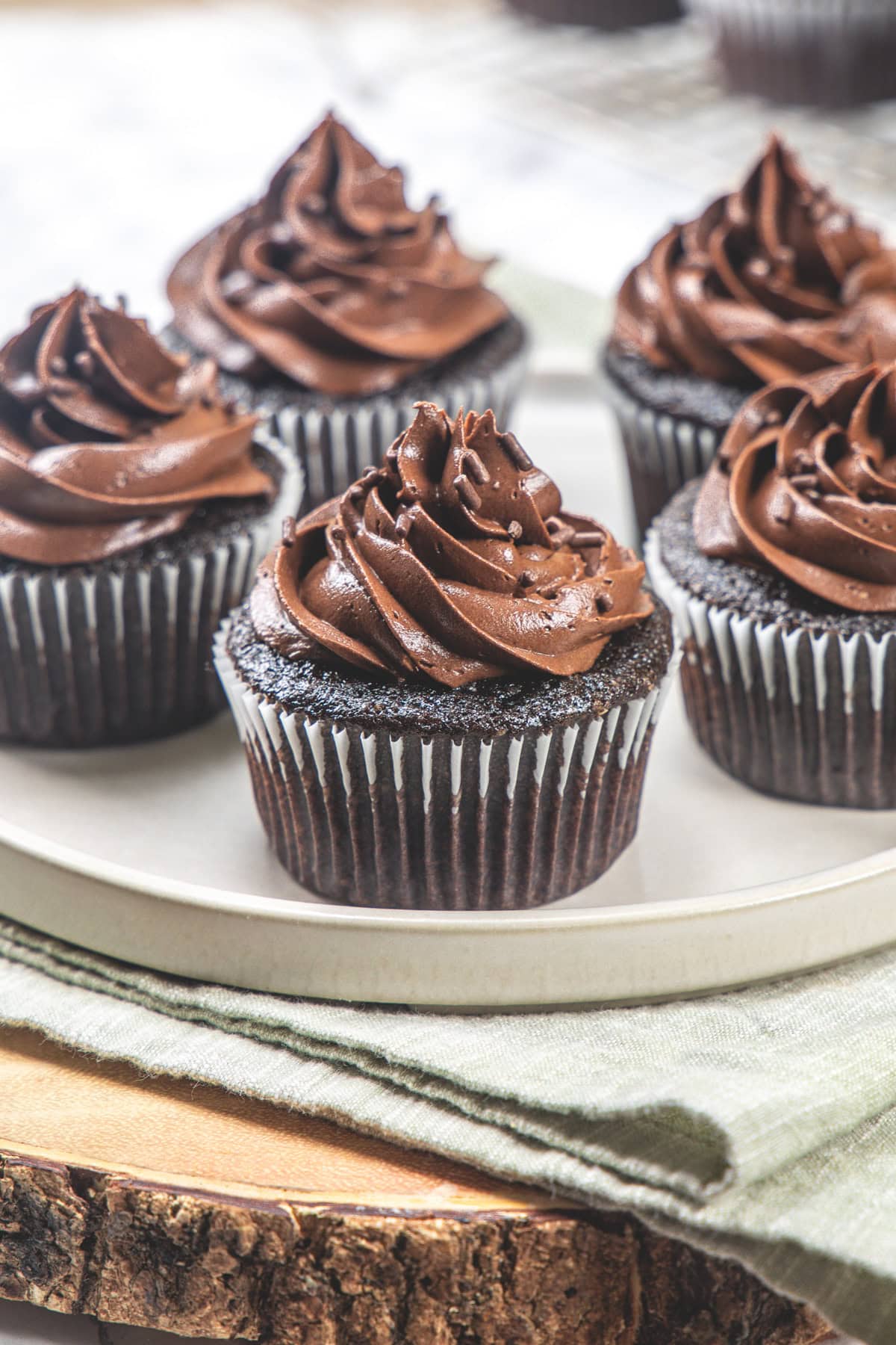 5 eggless chocolate cupcakes in a plate with napkin and wooden board under the plate.