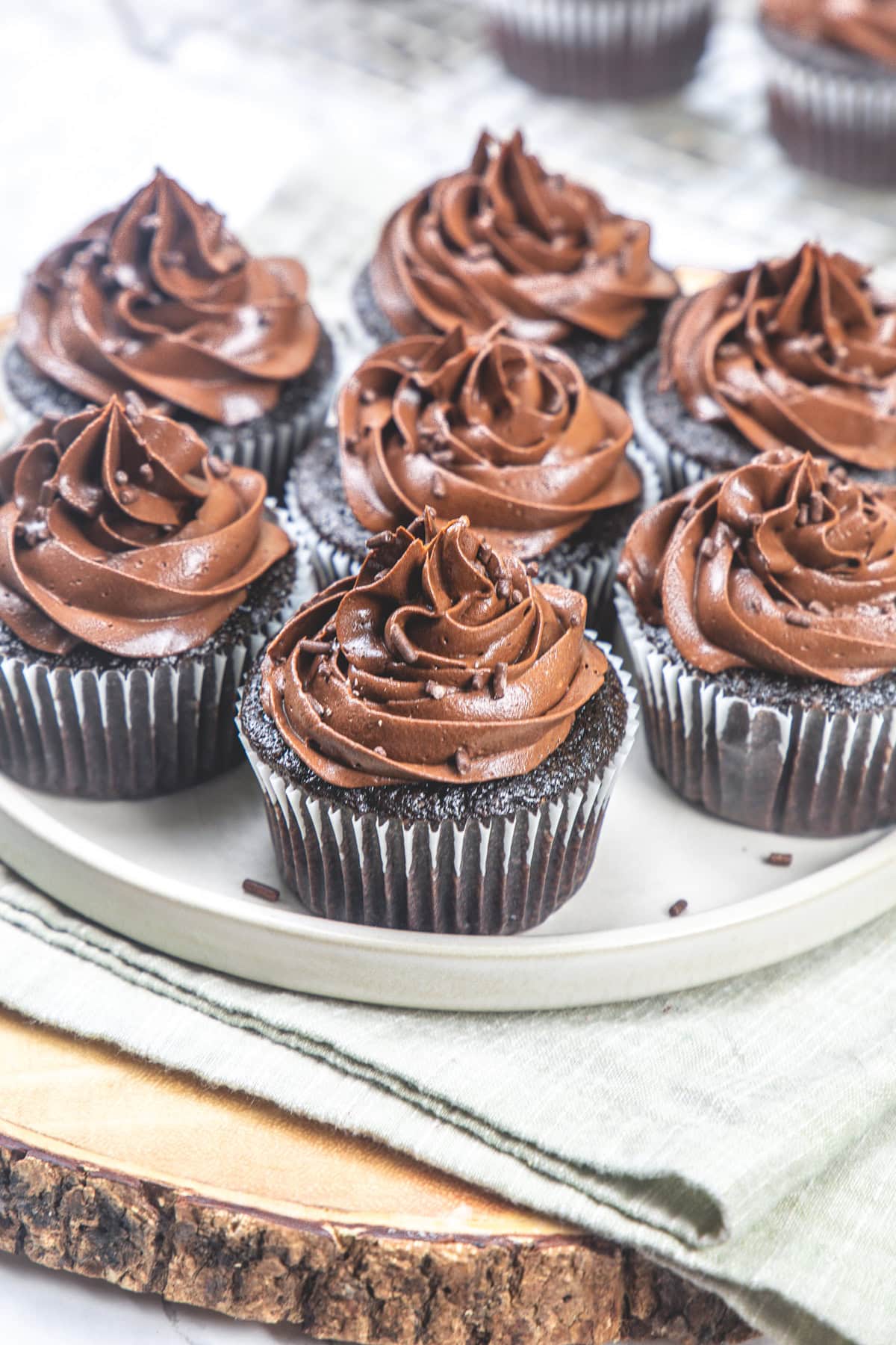 7 eggless chocolate cupcakes with chocolate buttercream frosting on a plate.