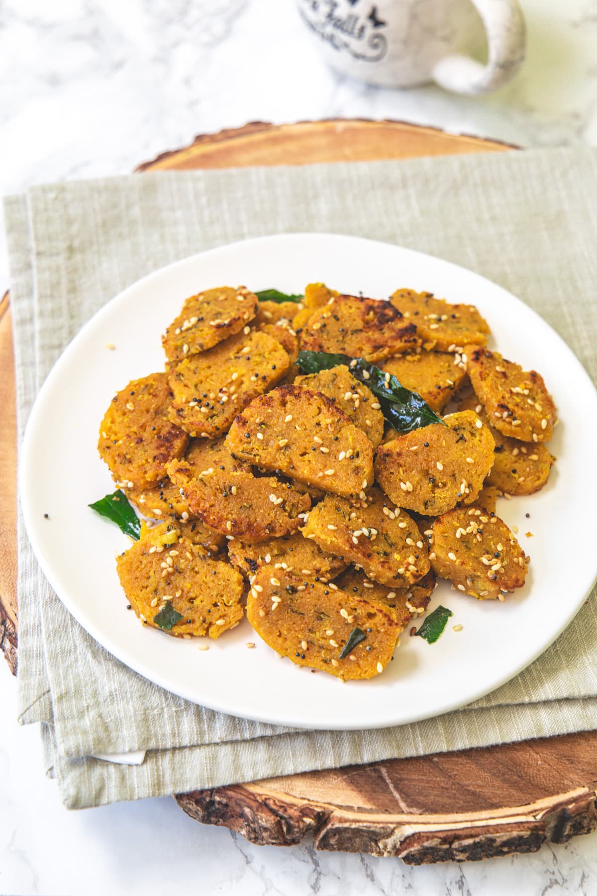 Dudhi muthiya in a white plate with napkin under it and a cup in the back.