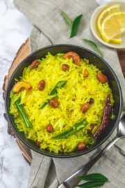 Lemon rice topped with peanuts, cashews, curry leaves with a spoon and lemon slices on the side