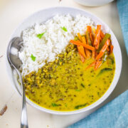A bowl of khatta moong with rice and carrot sambharo with spoon.