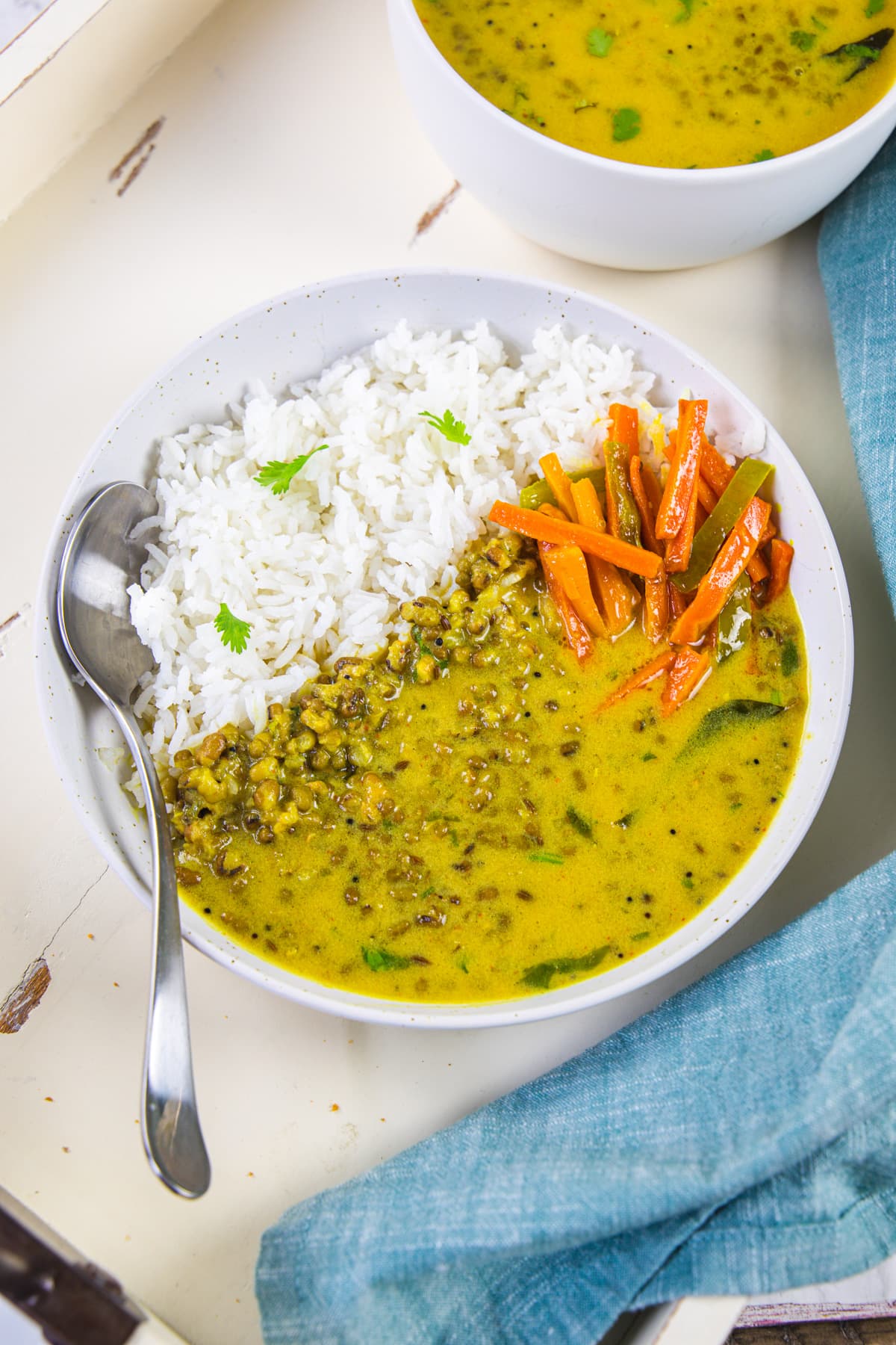 A bowl of khatta moong with rice and carrot sambharo with spoon.