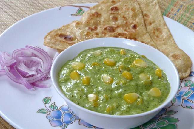 Sweet Corn Curry in a bowl with paratha and sliced onion on the side.