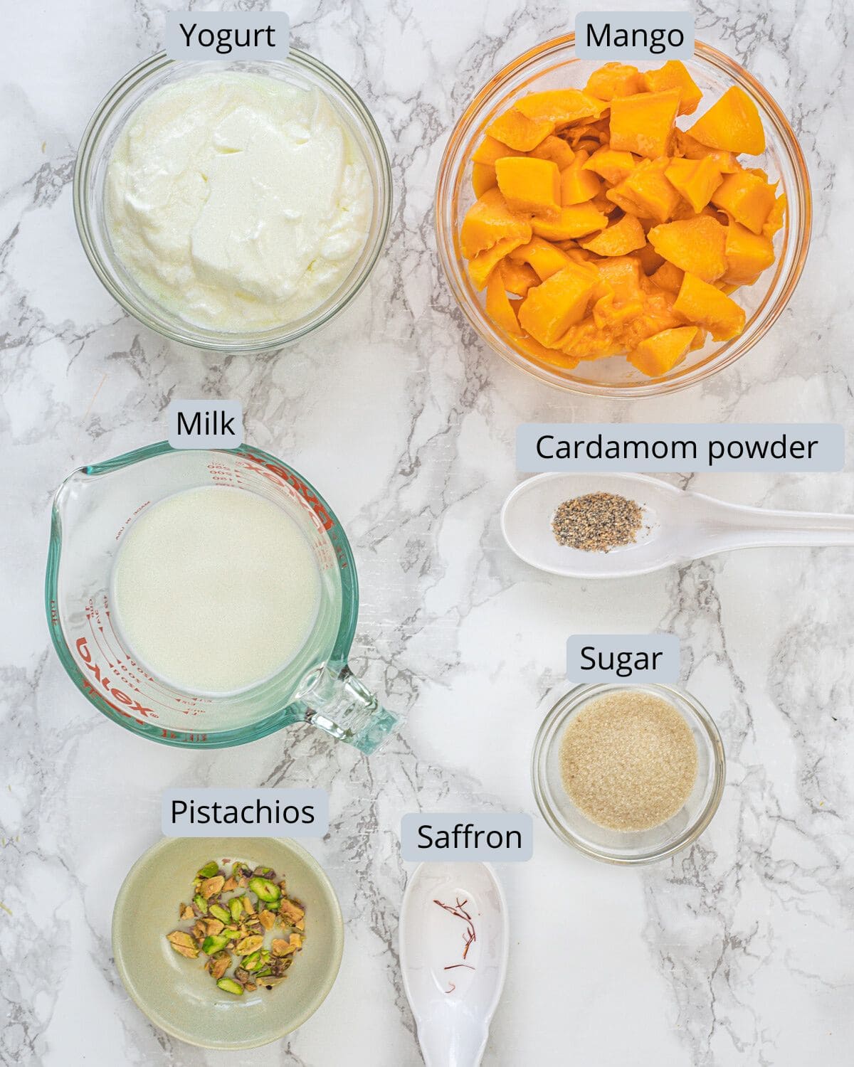 Mango lassi ingredients in bowls and cup with labels.