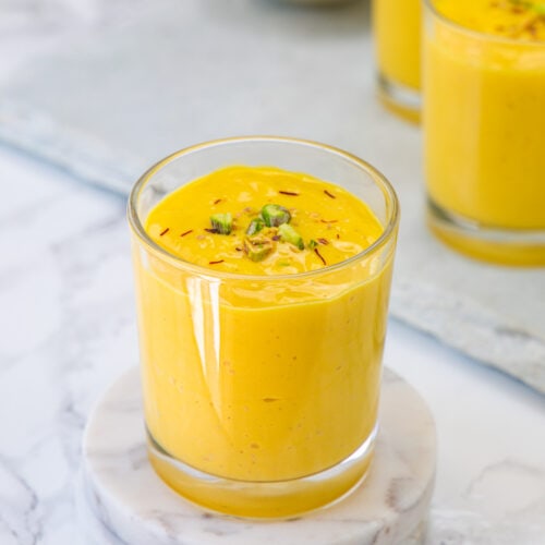 A glass of mango lassi garnished with saffron the pistachios.