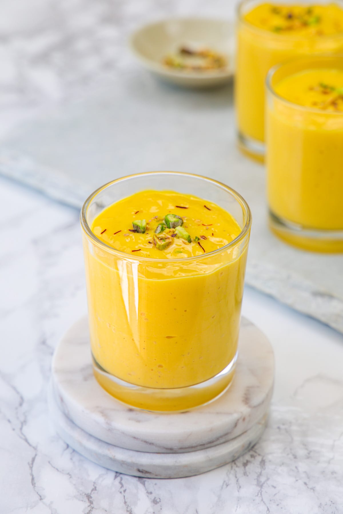 A glass of mango lassi garnished with saffron the pistachios.
