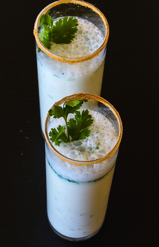 Masala chaas in 2 talls glasses with garnish of cilantro leaves