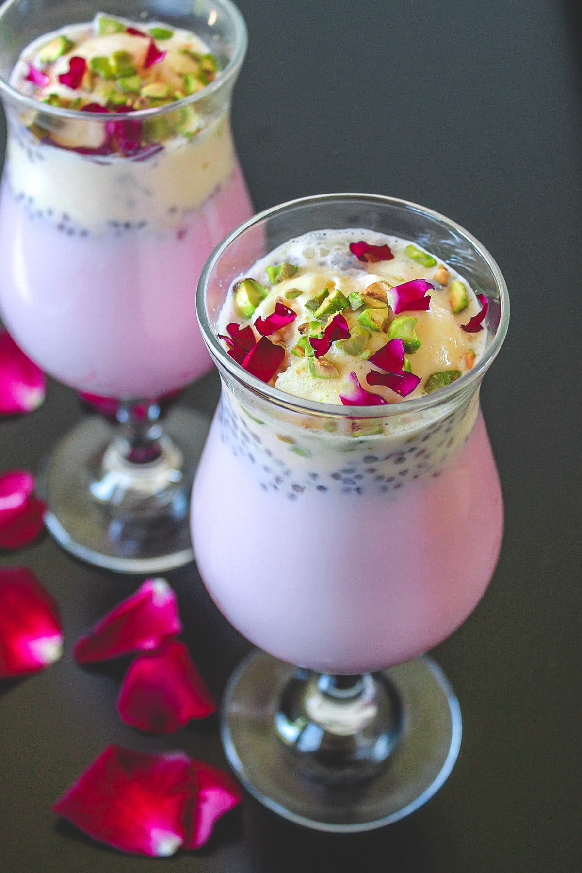 2 glasses of falooda garnished with pista and rose petals.