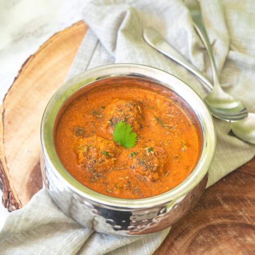 Lauki kofta curry served in a steel serving bowl with spoons on the side and napkin under the bowl.