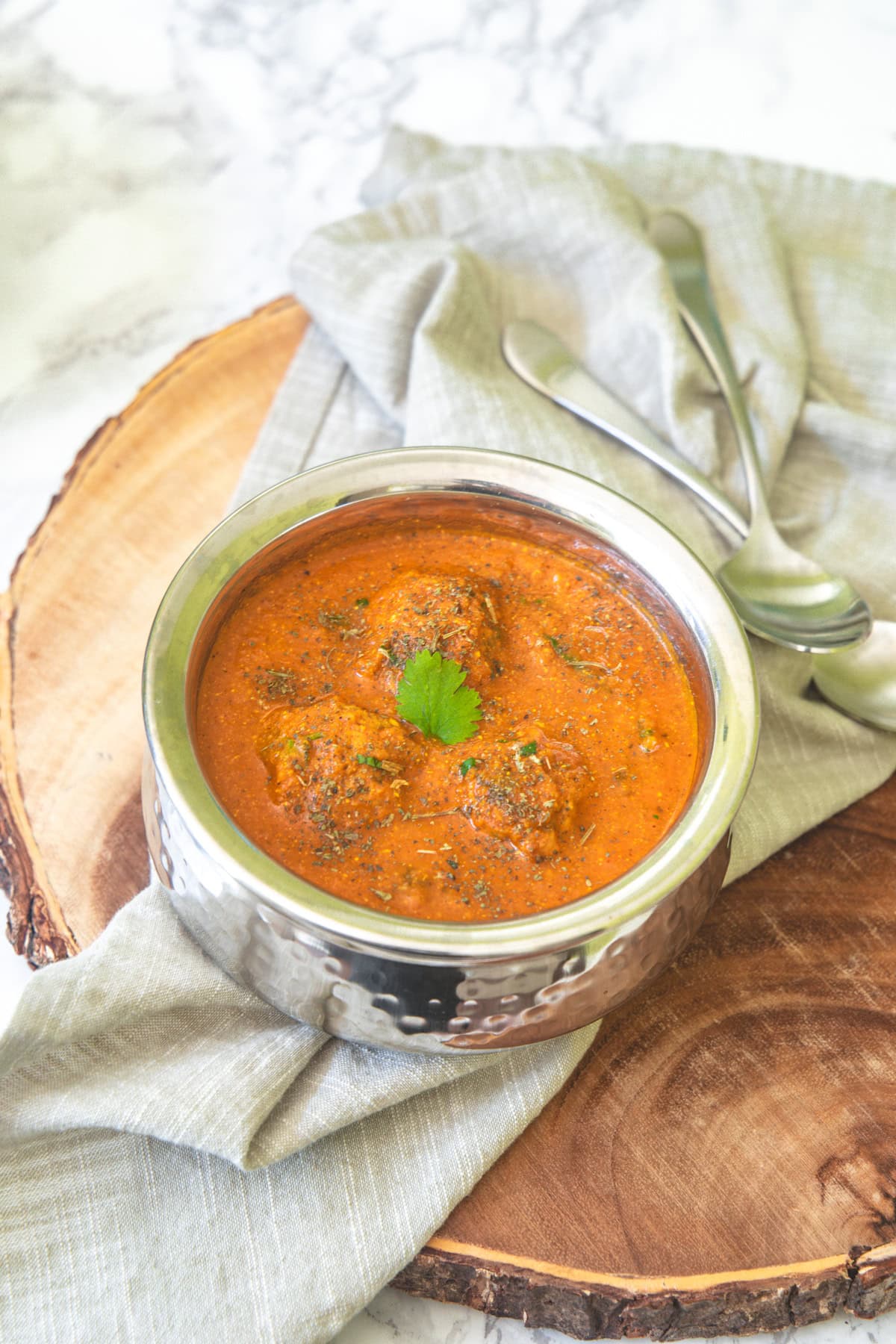 Lauki kofta curry served in a steel serving bowl with spoons on the side and napkin under the bowl.