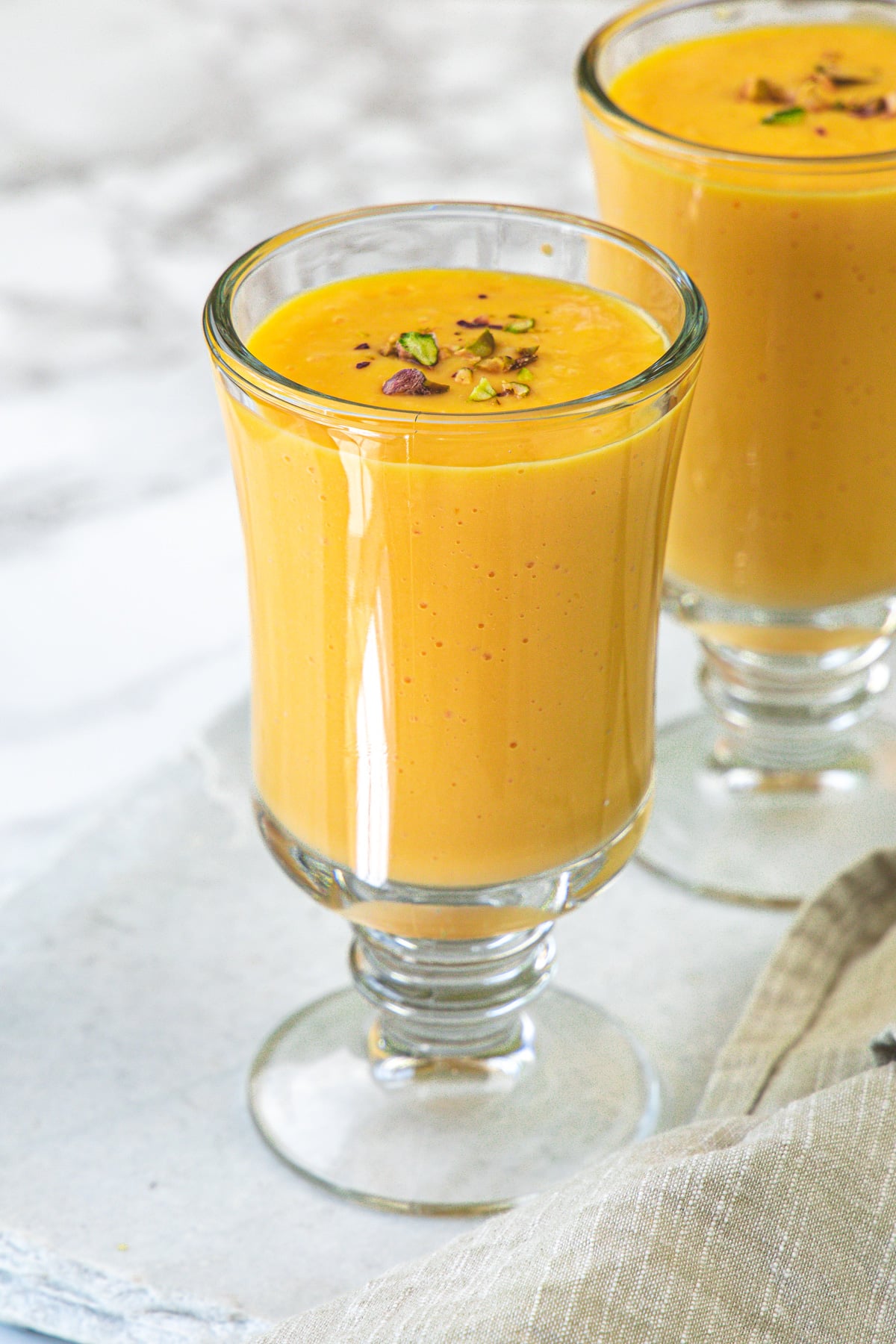 2 glasses of mango milkshake garnished with pistachios.