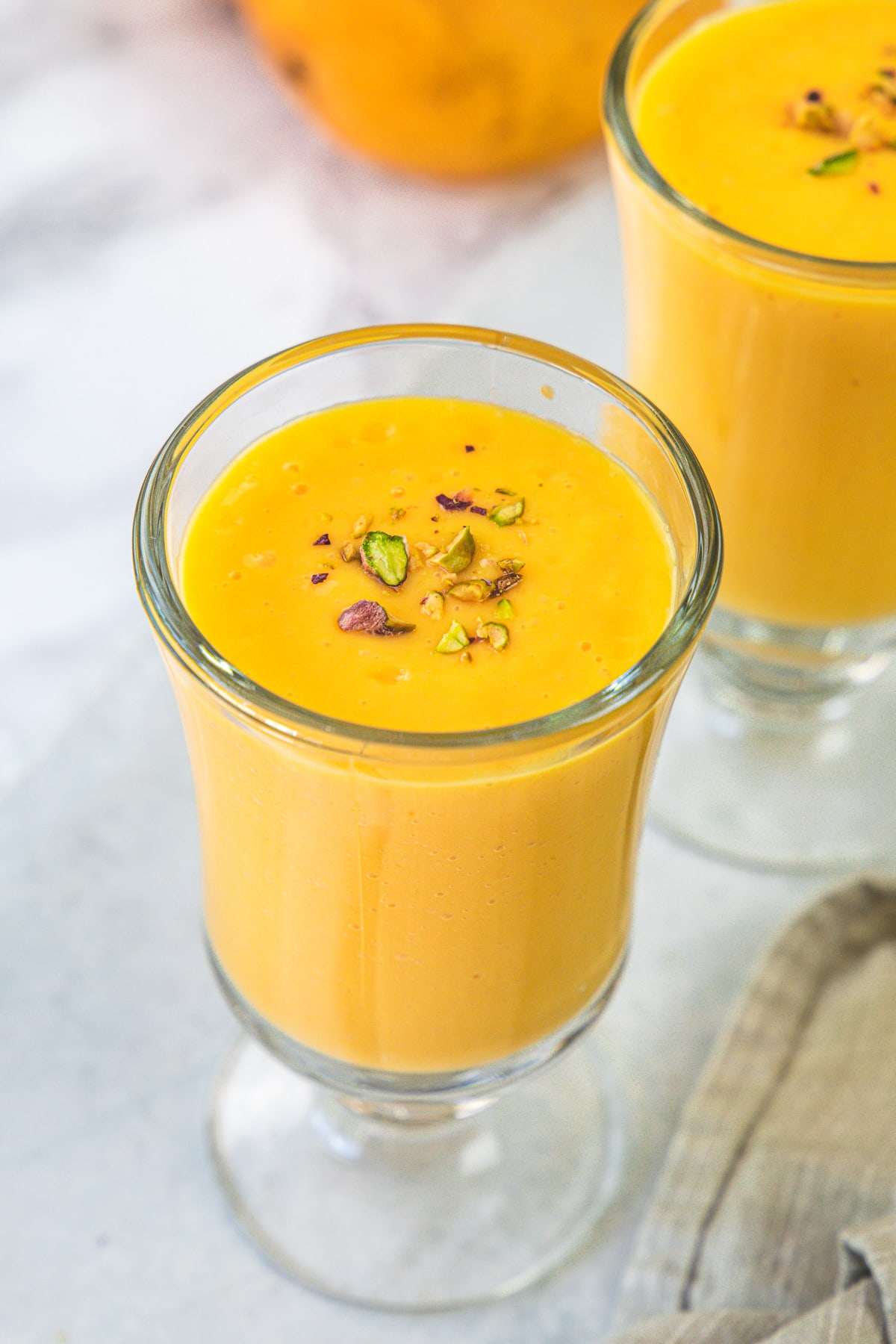A glass of mango milkshake topped with chopped pistachios.