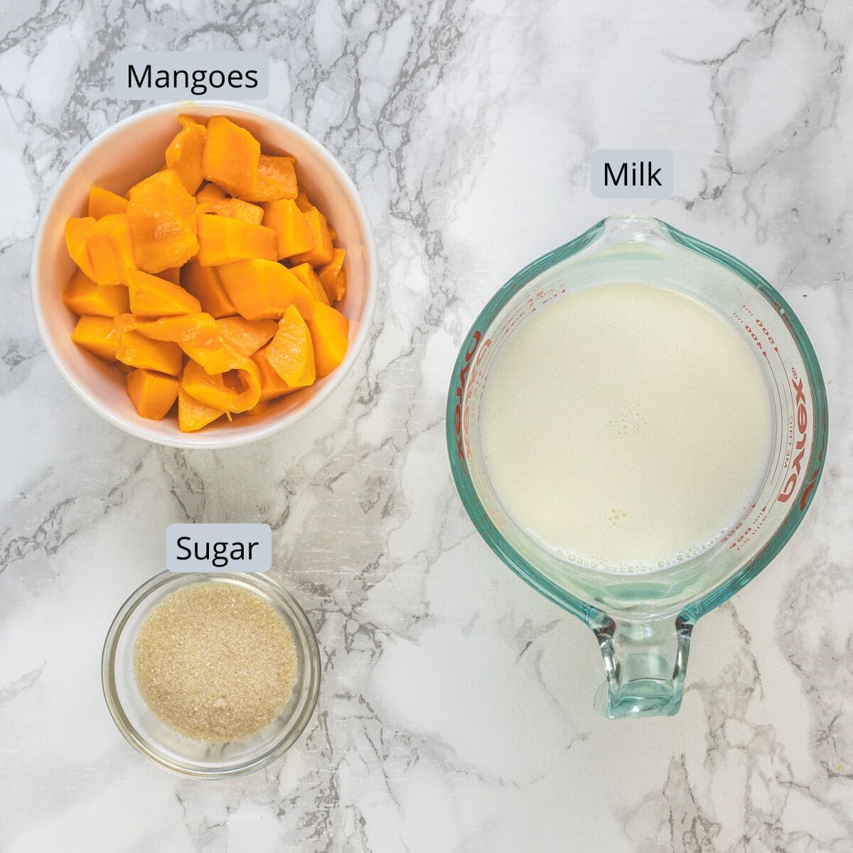 Mango milkshake ingredients in bowls and a cup with labels.