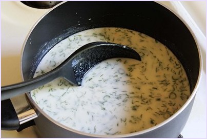 Suva kadhi mixture into a pan with spoon inside.