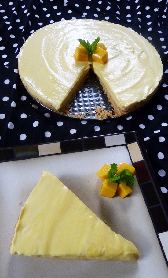 Mango cheesecake slice in a plate with mango pieces and mint leaves.