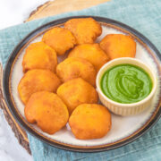 Aloo pakora in a plate with green chutney in a small bowl.