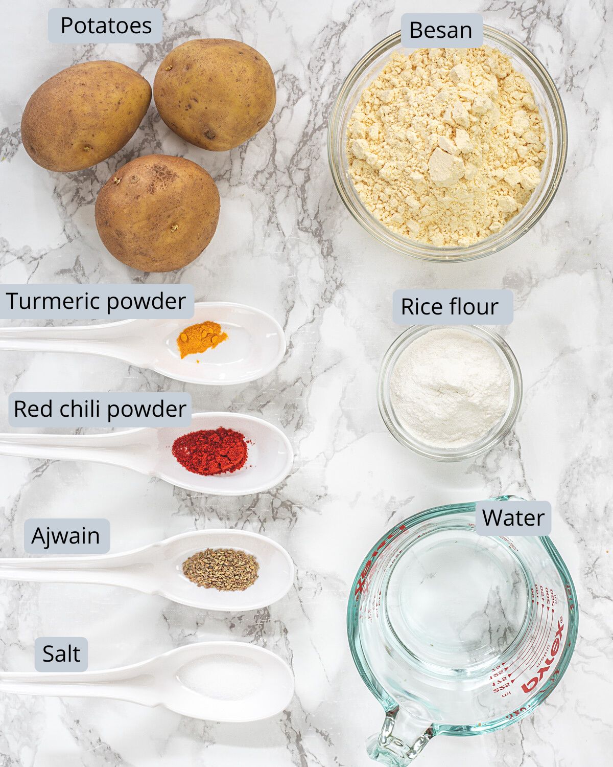 Aloo pakora ingrediets in bowls and spoons with labels.