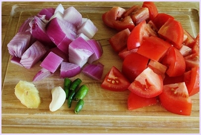 Onion, tomato, ginger, garlic and green chili on a chopping board.