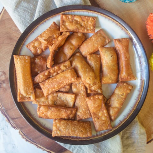 A plate of namak para with a napkin and wooden board under the plate.