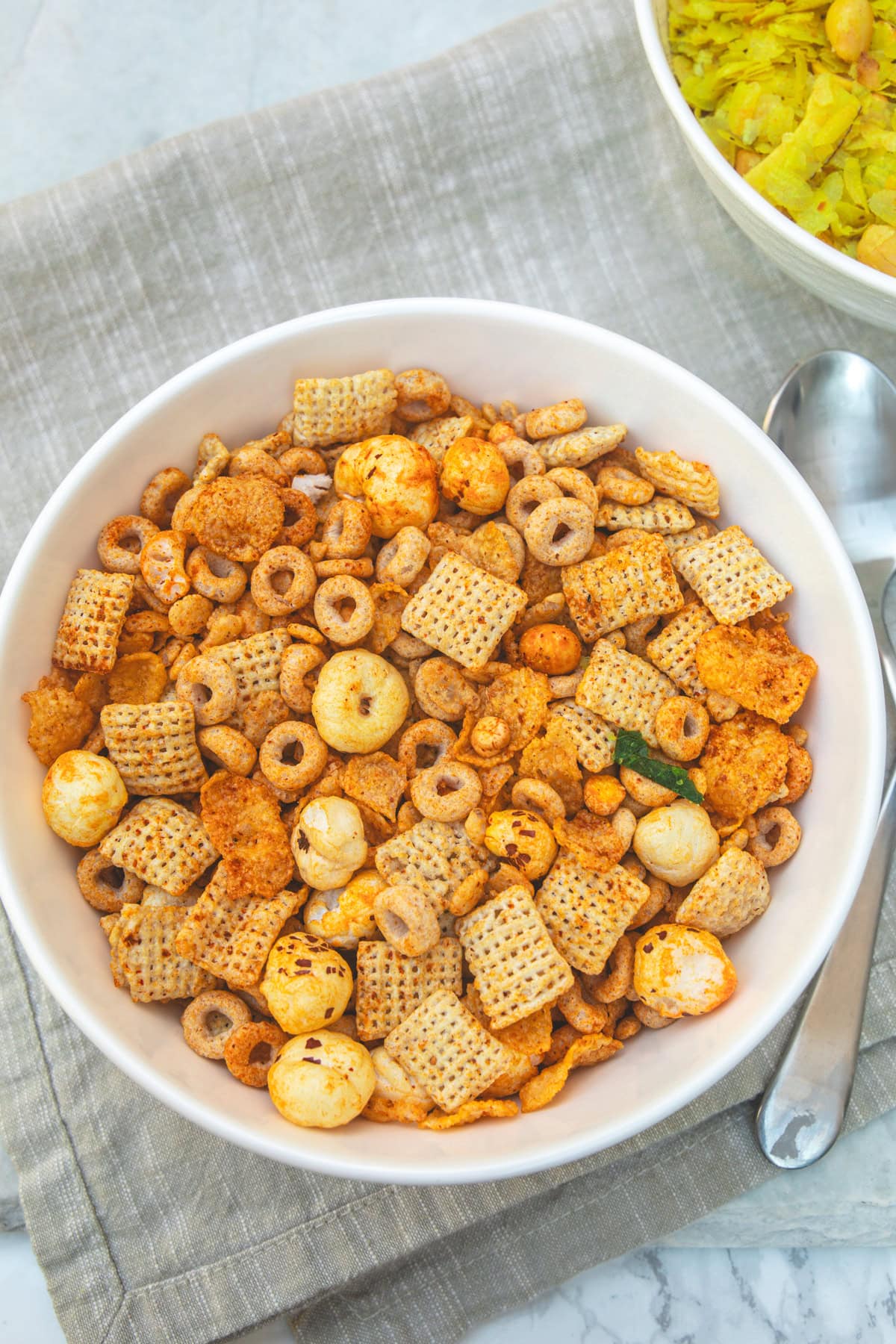 A bowl of cereal chevdo with spoons on the side.