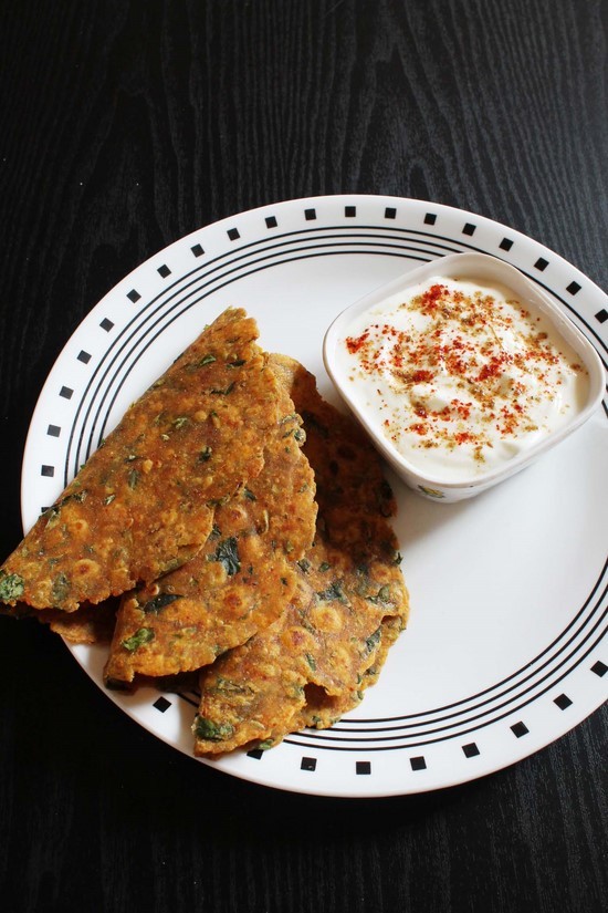 3 thepla folded in half in a plate and a bowl of yogurt on side.