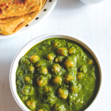 Chana palak bowl with paratha and cucumber, tomato in the back.