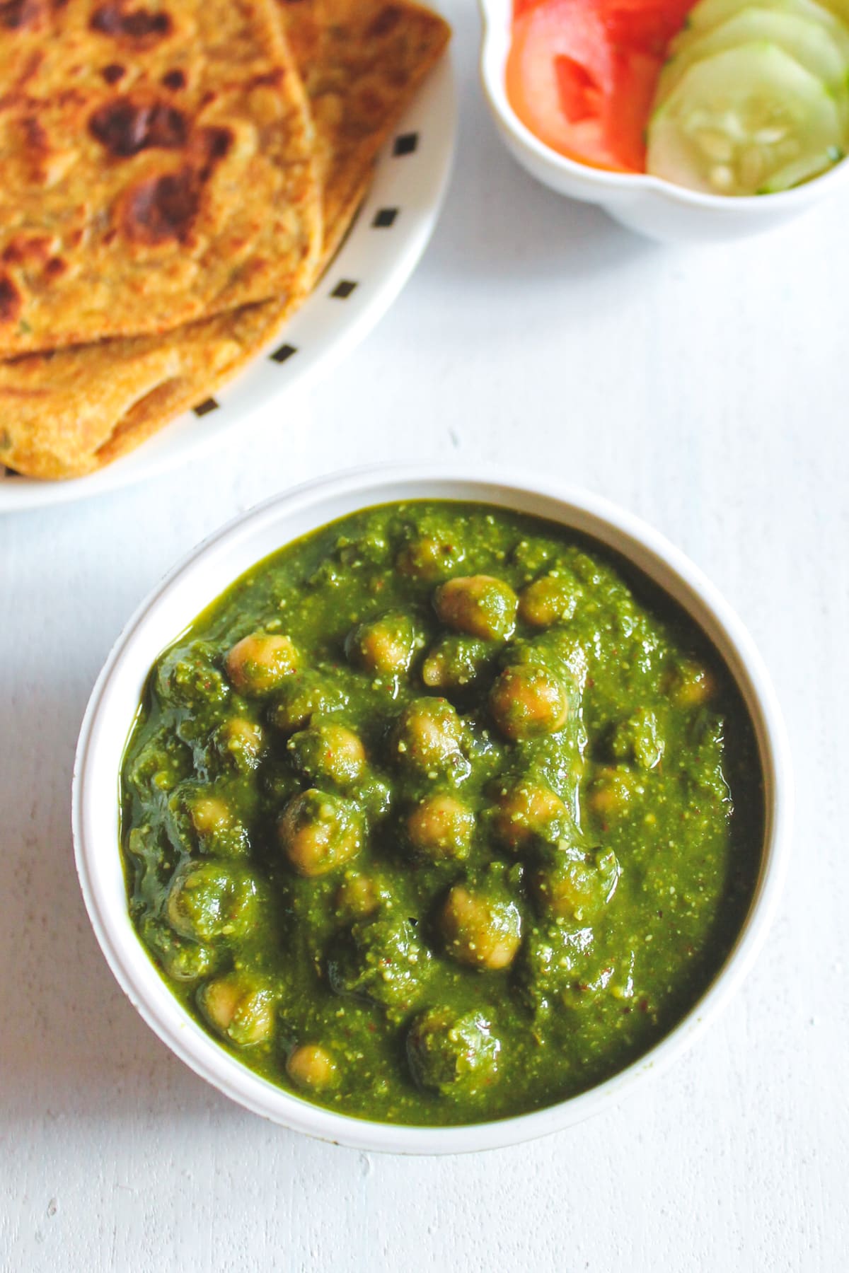 Chana palak bowl with paratha and cucumber, tomato in the back.