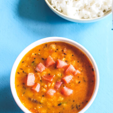 A bowl of tomato dal with a plate of rice in the back.