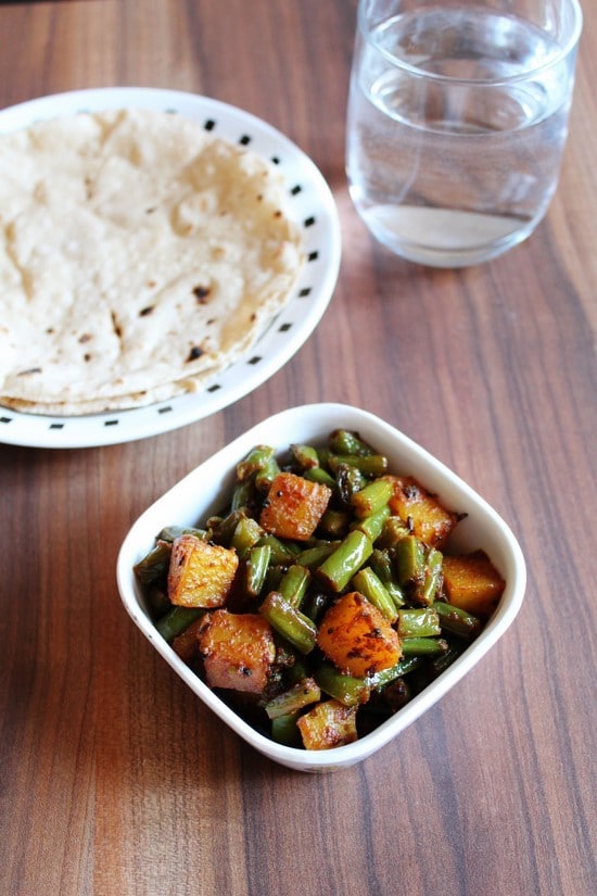 Aloo Beans sabzi served in a bowl with roti and a glass of water in the back.