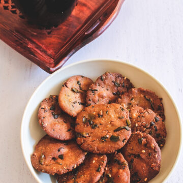 Bajri vada in a plate with a cup of tea in the back.