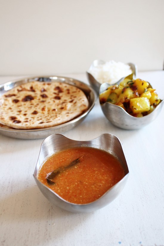 Katachi Amti in a bowl with puran poli, batata bhaji and rice in the back.