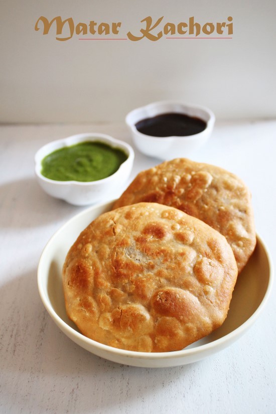 2 matar kachori in a plate with 2 bowls of chutney in the back.