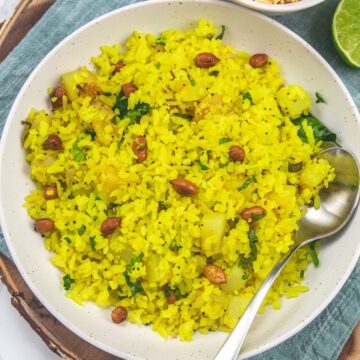 Batata poha served in a plate with a spoon with side of sev.