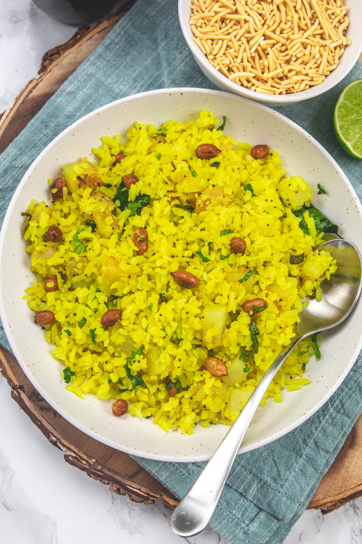 Batata poha served in a plate with a spoon with side of sev.