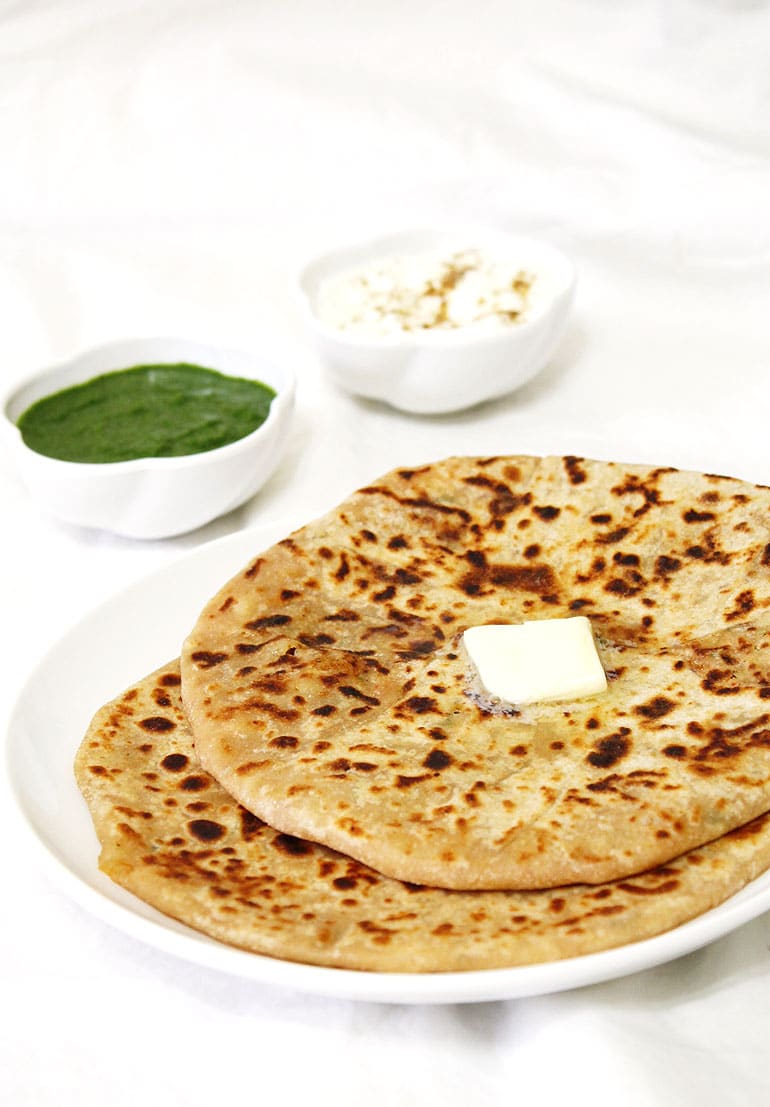 Aloo paratha topped with butter and side of green chutney and yogurt.