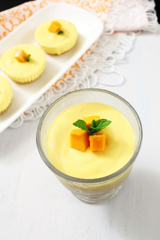 Mango cheesecake in a cup with a few mini ones in the plate.