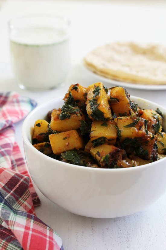 Aloo methi sabzi in a bowl with roti and chass in the back.