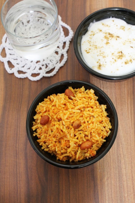 Vagharelo Bhaat in a bowl with a glass of water and a bowl of yogurt in the back.