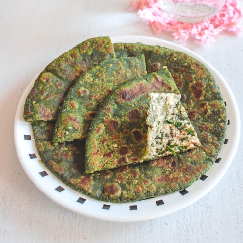 Palak paneer paratha in a plate and 3 triangle pieces with 1 piece is slightly open.