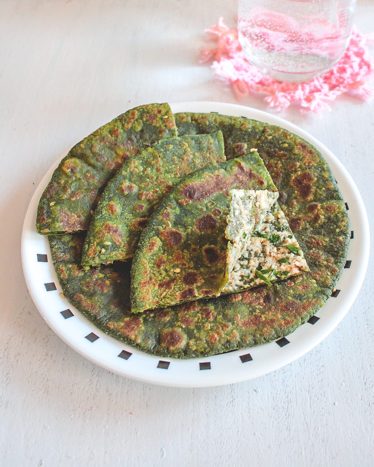 Palak paneer paratha in a plate and 3 triangle pieces with 1 piece is slightly open.