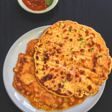 2 besan chilla on the plate with green chutney and ketchup on the side.