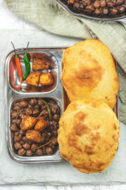 A plate of chole bhature with green chilies on the side.
